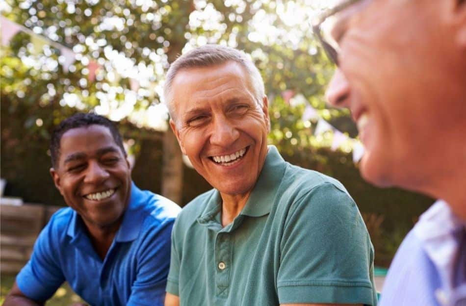 A group of middle-aged men sitting around outside talking to one another and smiling